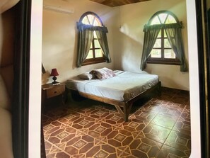 A bedroom with a single bed, two windows with curtains, a nightstand, and a patterned floor. - Very comfortable home located on a private lot inside the Hacienda Iguana (Rivas)