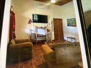 A living room with two sofas, a TV mounted on the wall, a wooden door, and a small table. - Very comfortable home located on a private lot inside the Hacienda Iguana (Rivas)