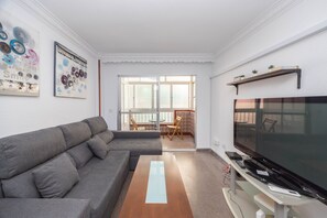 Ein Wohnzimmer mit grauem Sofa, Fernseher und Couchtisch aus Holz.
