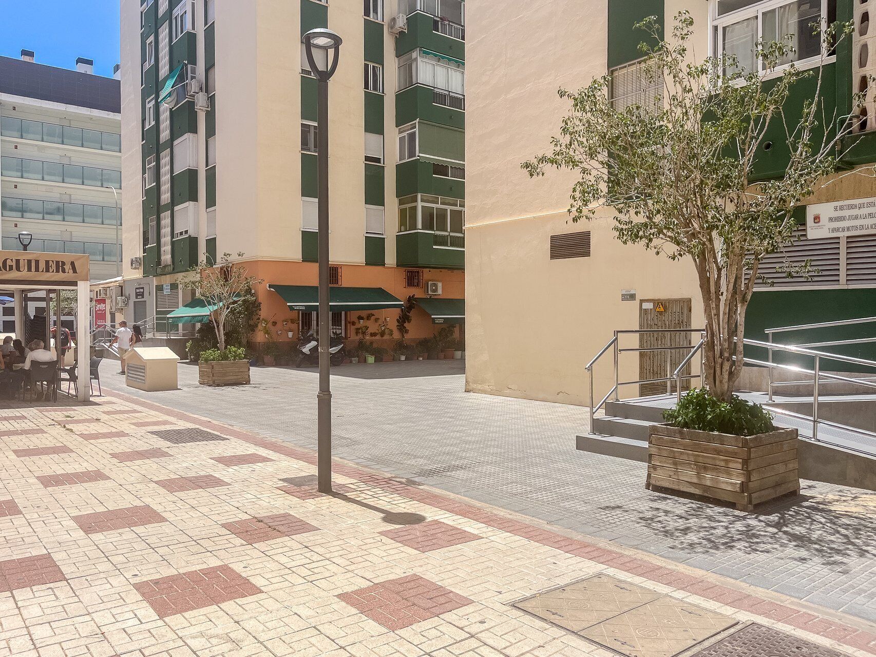 Un edificio con fachada verde y color beige, zona de estar al aire libre y jardinera con un árbol.