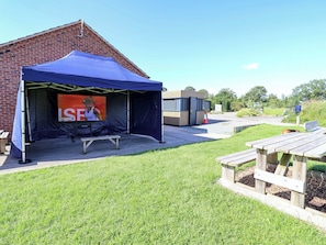 A brick building with a blue tent, a bench, and a picnic table. - Escape II (Northwich)
