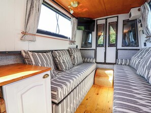 A cozy RV interior with a sofa, a small table, and a window with curtains. - Escape II (Northwich)