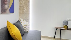 A modern living room with a grey sofa, a yellow pillow, a small table with a lamp, and a painting on the wall. - ELORO - Guest Houses (Noto)
