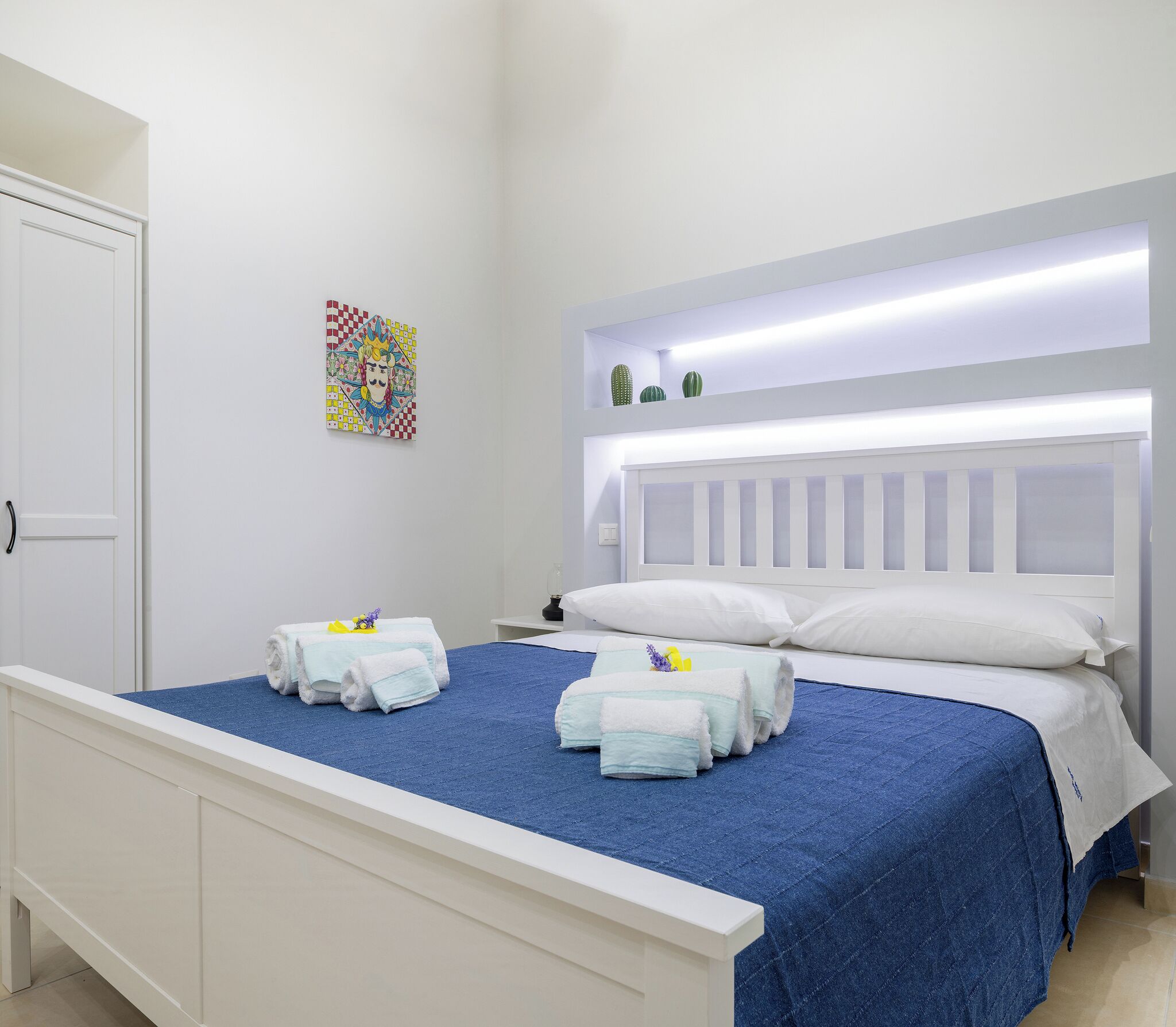 Une chambre à coucher avec un lit, une tête de lit blanche et un luminaire fixé au mur.