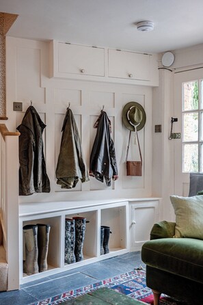 Ein Zimmer mit einer weißen Bank, Stiefeln, einem grünen Stuhl und einem Hut an der Wand.