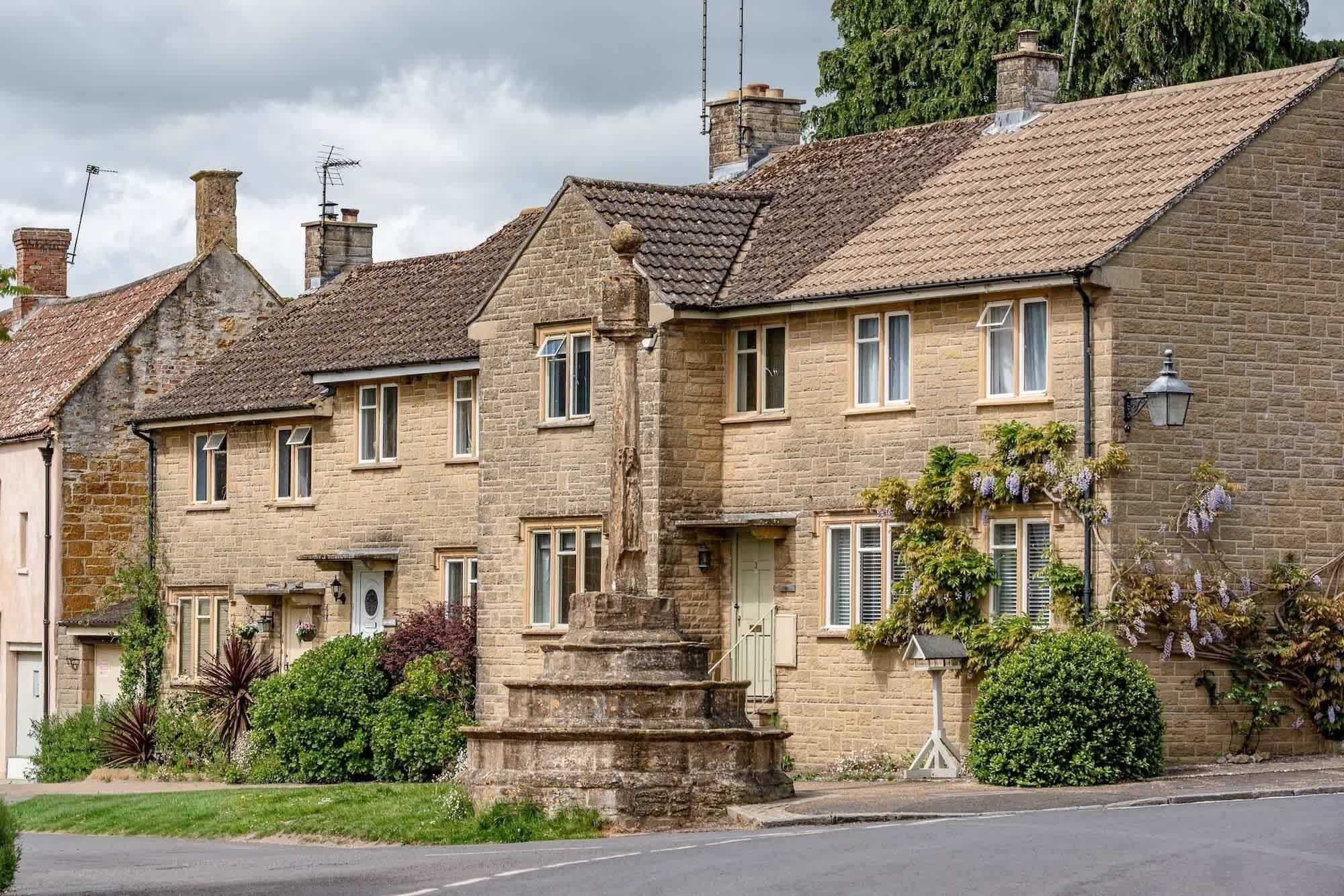A row of stone houses with traditional pitched roofs, a central stone monument, and a well-maintained garden.