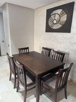A dining area with a rectangular table and six chairs, a decorative wall piece above the table, and a light-colored floor. - Reda's'Apparts (Prestigia—Unlimited Fiber Wi-Fi) (Fès)