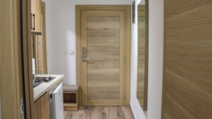 A narrow hallway with a wooden door, a small bench, and a kitchen area with a dishwasher. - Mountain Bliss Spa Resort – Luxury Apartments with Sauna & Jacuzzi (Kolasin)