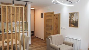 A modern interior with a wooden partition, a sofa, a dining table, and a radiator. - Mountain Bliss Spa Resort – Luxury Apartments with Sauna & Jacuzzi (Kolasin)