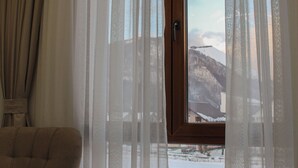 A room with a sofa, a wooden table, and a window with sheer curtains. - Mountain Bliss Spa Resort – Luxury Apartments with Sauna & Jacuzzi (Kolasin)