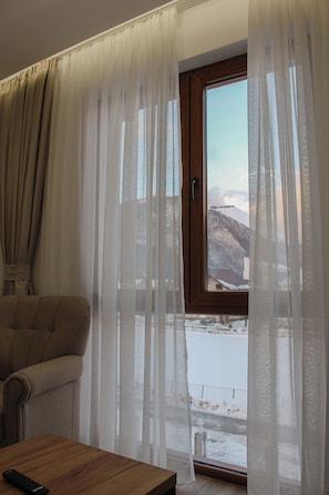 A room with a sofa, a wooden table, and a window with sheer curtains.