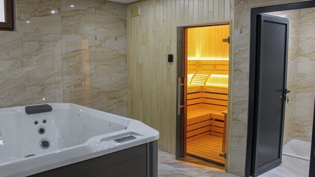 A bathroom with a large bathtub, a wooden sauna, and a door leading to a shower area. - Mountain Bliss Spa Resort – Luxury Apartments with Sauna & Jacuzzi (Kolasin)