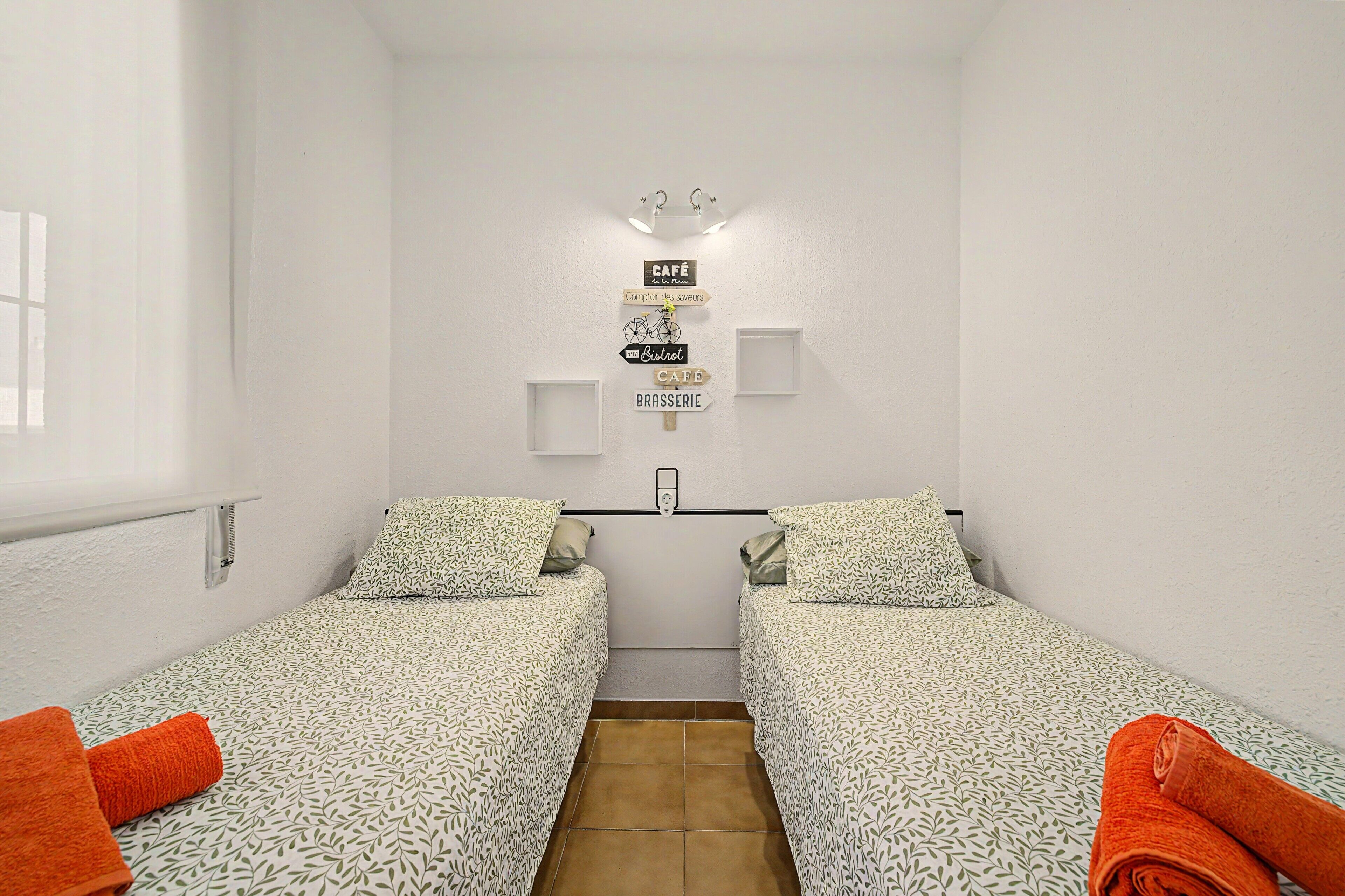 A small, clean room with two single beds, a wall-mounted light, and a sign indicating a cafe.