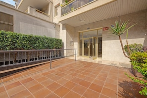 Ein Gebäudeeingang mit gefliestem Patio, einer Hecke und einer Palme.