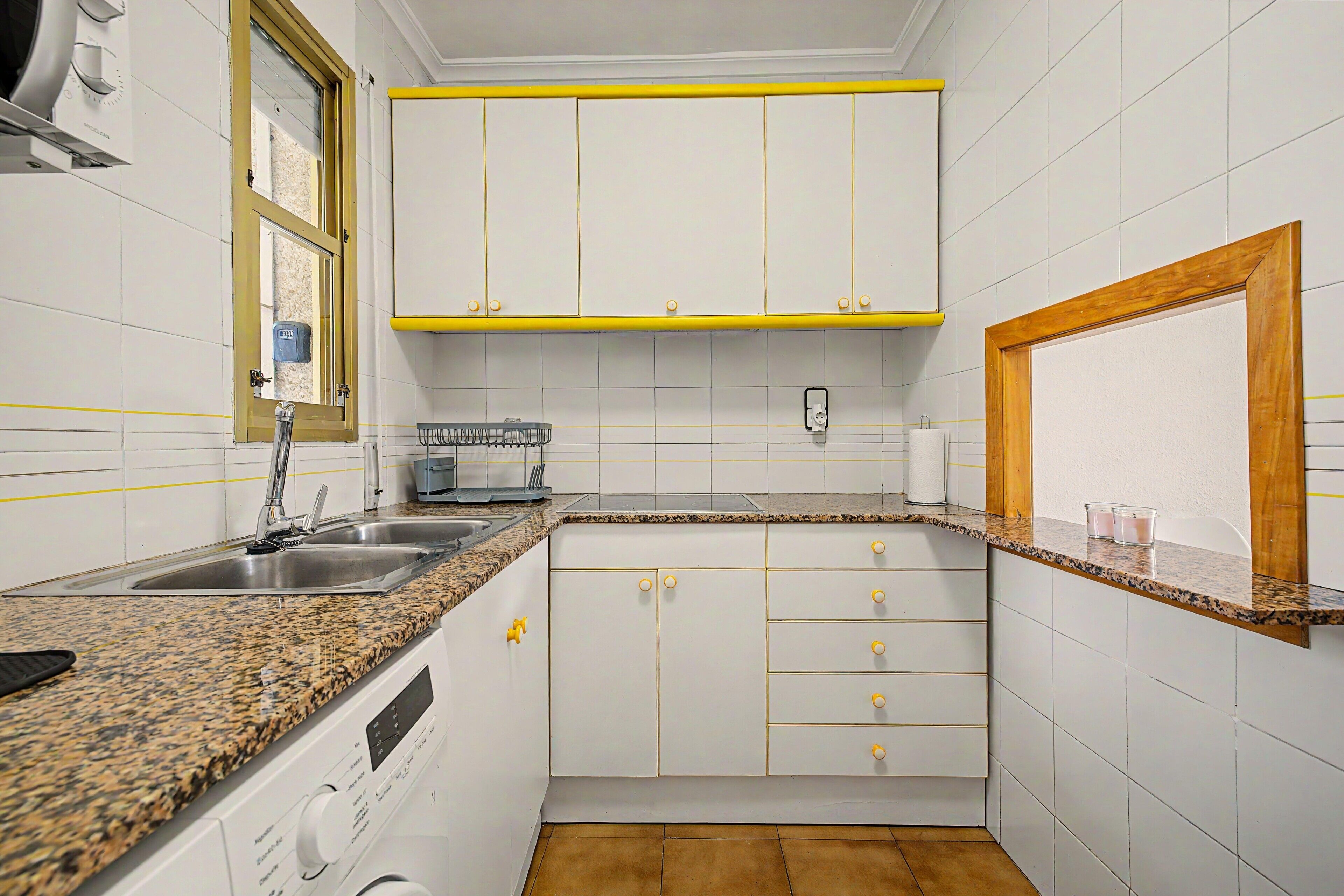 A kitchen with white cabinets, a granite countertop, a built-in oven, and a window with a yellow frame.