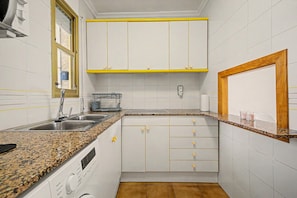 Eine Küche mit weißen Schränken, einer Arbeitsplatte aus Granit, einem eingebauten Backofen und einem Fenster mit gelbem Rahmen.