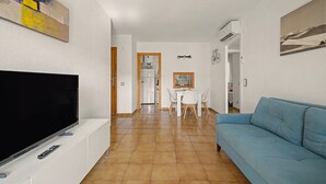 Sala de estar con televisor, sofá azul, comedor con mesa y sillas, y cocina al fondo.