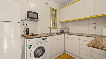 A compact kitchen with white cabinets, a built-in microwave, a washing machine, and a granite countertop.