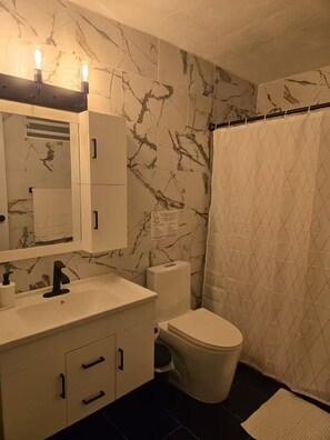 Un baño con salpicadero de mármol, un lavabo blanco con grifo negro, inodoro y cortina de ducha.