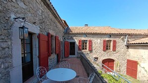 A courtyard with stone walls, red shutters, and white metal furniture. - Authentic farmhouse at an elevation of 800 meters between Larzac and the Cévennes; sleeps 15 (Campestre-et-Luc)