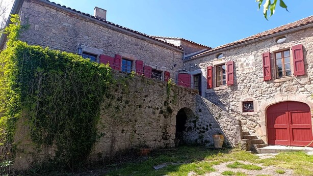A stone building with red shutters, a stone archway, and a small garden area. - Authentic farmhouse at an elevation of 800 meters between Larzac and the Cévennes; sleeps 15 (Campestre-et-Luc)
