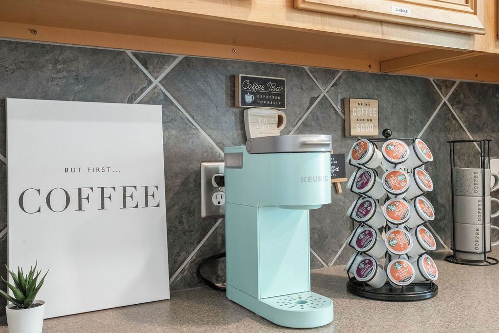 A coffee station with a Keurig machine, a coffee pod dispenser, and a sign that reads 'Coffee Bar Espresso Yourself'.