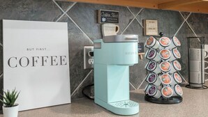 Ein Kaffee-Bereich mit einer Keurig-Maschine, einem Kapselspender und einem Schild mit der Aufschrift 'Coffee Bar Espresso Yourself'.