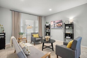 A modern living room with a sofa, armchair, and coffee table, a bookshelf, and a painting on the wall. - Near Austin ~ Private Pool ~ Game Room ~ Fire Pit ~ Waterparks (Pflugerville)