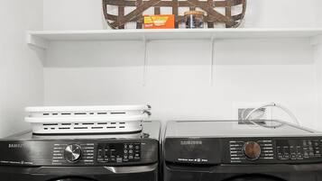 A laundry area with two front-loading washing machines, a shelf with a decorative metal piece, and a box of laundry detergent.
