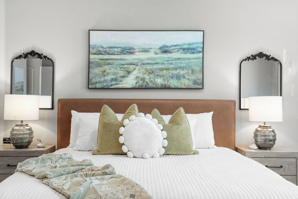 A bedroom with a large bed, two nightstands, a painting, and two mirrors.