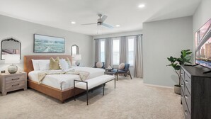 Ein Schlafzimmer mit einem Bett, Nachttischen, einem Sessel, einem Fernseher und einem Deckenventilator.