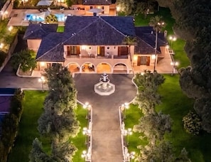 A large, two-story building with a central courtyard, multiple entry points, and a well-lit outdoor area. - Luxurious, swimming pool, home theater, elevator, sauna, fitness area, game room (Mascalucia)