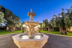 A fountain with multiple tiers and statues, surrounded by trees and a well-maintained lawn. - Luxurious, swimming pool, home theater, elevator, sauna, fitness area, game room (Mascalucia)