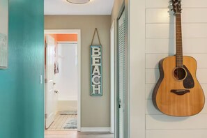 Ein Flur mit einer türkisfarbenen Tür, einer an der Wand befestigten Gitarre und einem Schild mit der Aufschrift 'BEACH'.