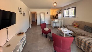 A living room with a TV, red chairs, a sofa, a dining table, and a kitchen in the background. - Apartment with garden in Saint-Raphaël (Saint-Raphaël)