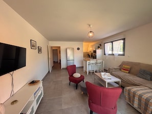 A living room with a TV, red chairs, a sofa, a dining table, and a kitchen in the background. - Apartment with garden in Saint-Raphaël (Saint-Raphaël)
