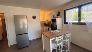 A compact kitchen with a refrigerator, a clock, a dining table with chairs, and a window with a view. - Apartment with garden in Saint-Raphaël (Saint-Raphaël)
