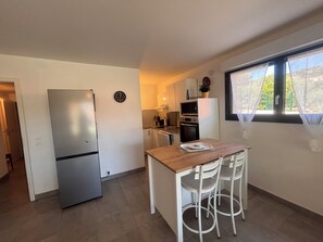 A compact kitchen with a refrigerator, a clock, a dining table with chairs, and a window with a view. - Apartment with garden in Saint-Raphaël (Saint-Raphaël)