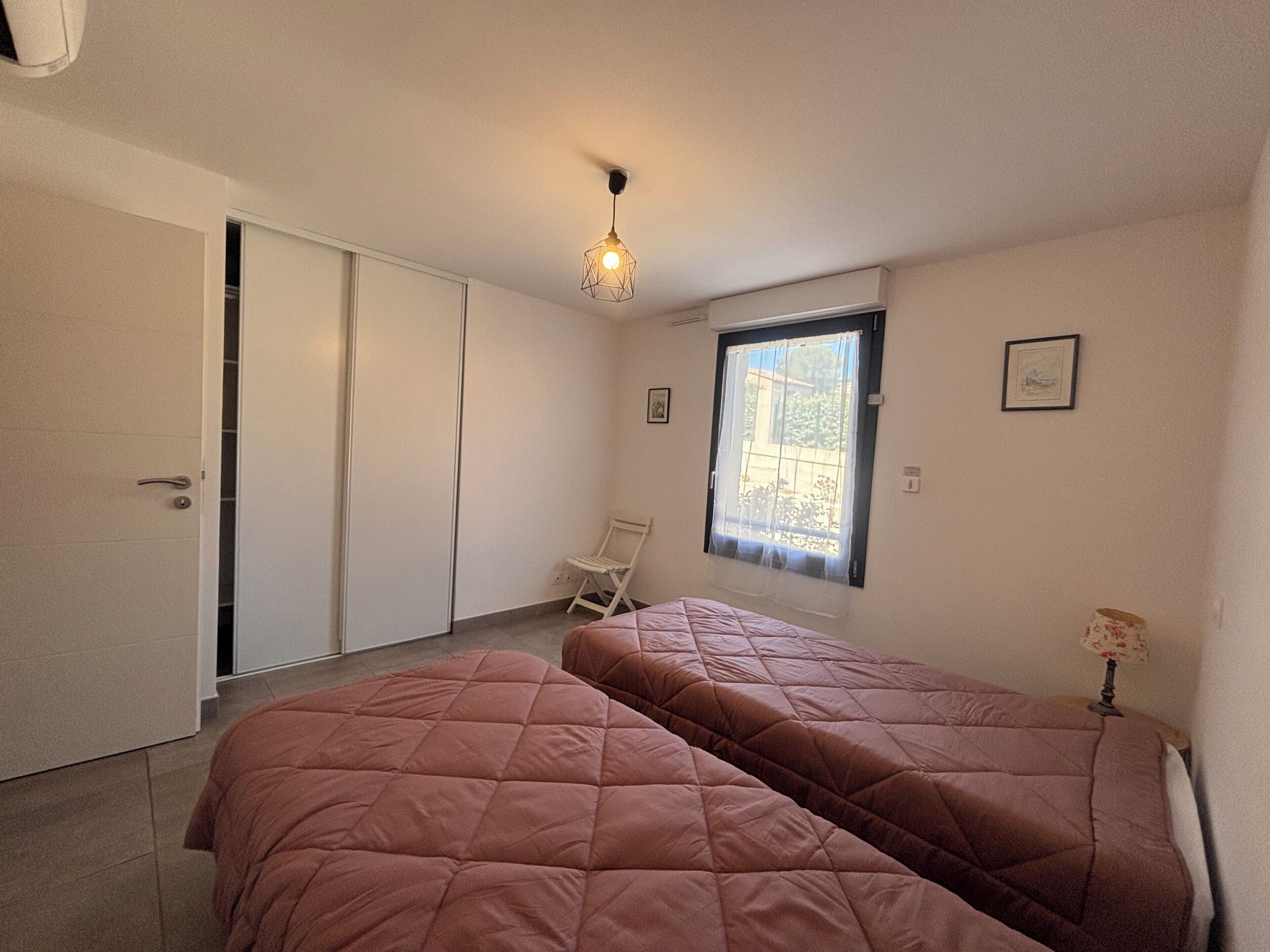 A bedroom with two beds, a window with a view, a chair, and a wardrobe.