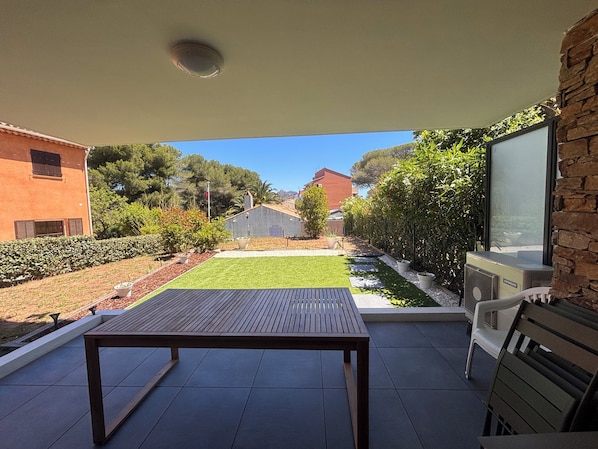A patio with a table and chairs, a view of a garden, and a building in the background. - Apartment with garden in Saint-Raphaël (Saint-Raphaël)
