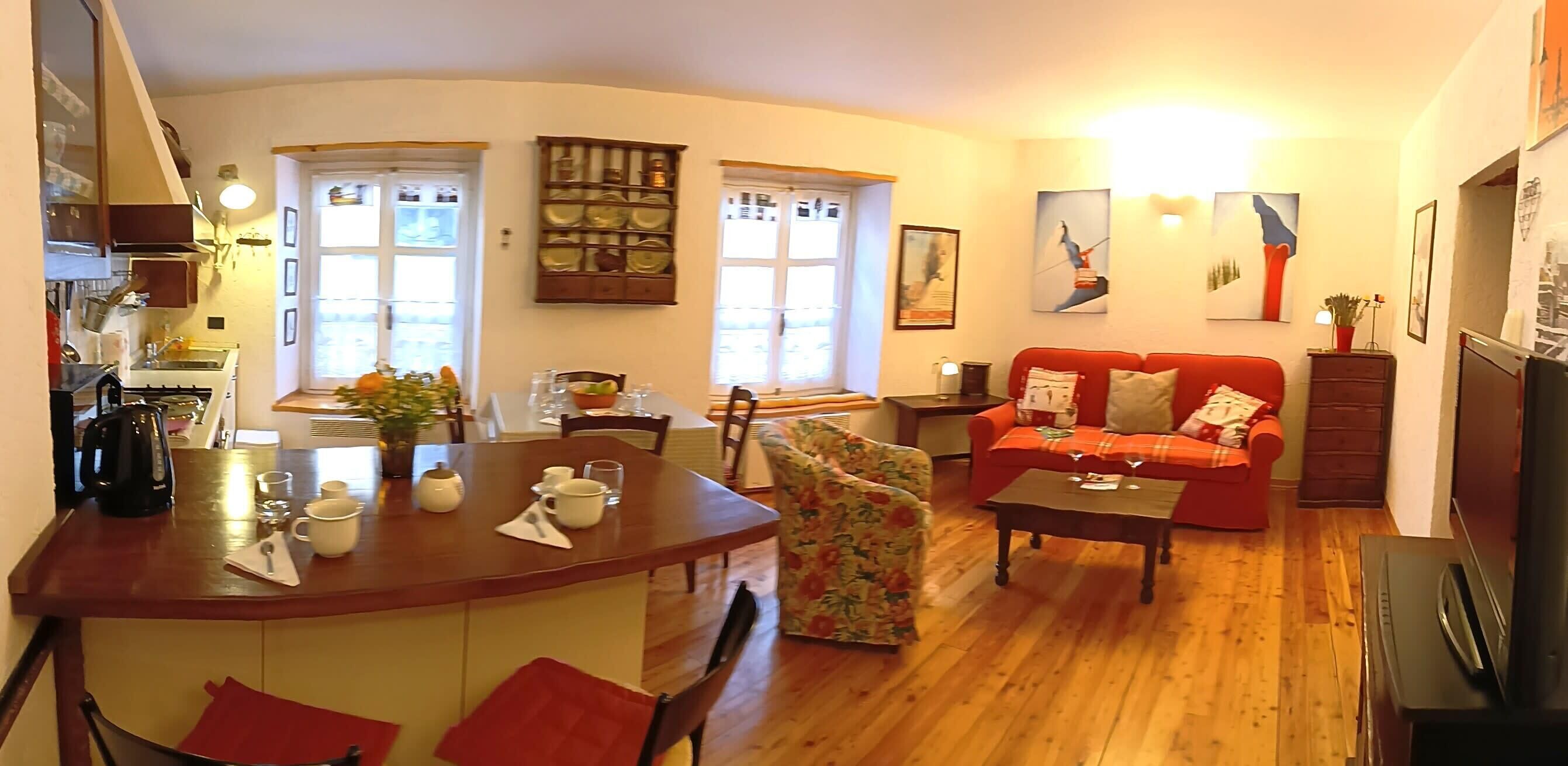 A cozy living room with a red sofa, a dining table with chairs, and a kitchen area with a stove.