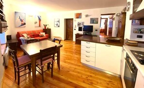 A compact kitchen with wooden flooring, a dining table with chairs, a sofa, and a TV. - House of the Temple - Perfect for 4 people (Briançon)