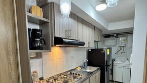 A modern kitchen with a gas stove, black refrigerator, wooden cabinets, and pendant lights. - Amber Sky Apartment (Armenia)