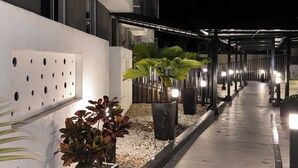 A nighttime outdoor corridor with a concrete floor, potted plants, and a building with a white facade and a perforated wall panel. - Amber Sky Apartment (Armenia)