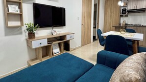 A modern living room with a flat-screen TV, a sofa, a coffee table, and a dining area with a table and chairs. - Amber Sky Apartment (Armenia)