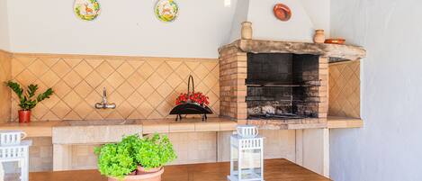 Una cocina con horno de ladrillo, plantas en macetas y una mesa de madera.