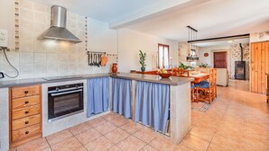 A kitchen with a built-in oven, a hanging range hood, and a dining area with a table and chairs. - Villa Ca Na Maria - By Dream Villas Pollensa (Pollensa)