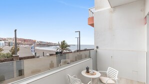 Un balcón con vistas a la playa, una mesa con sillas y una pequeña planta.