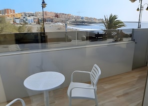 Ein Balkon mit Tisch und Stühlen mit Blick auf einen Strand und Gebäude.