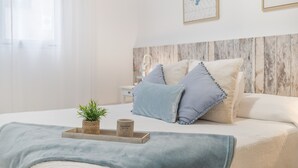 Una cama bien tendida con almohadas, una mesita de noche, una planta pequeña y una bandeja con una vela.